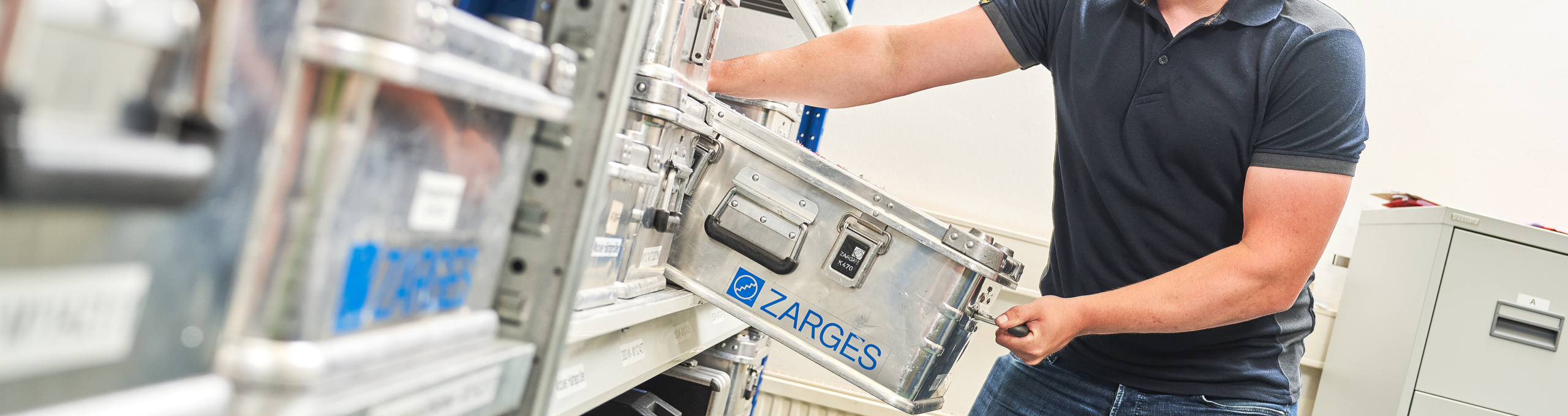 Regal mit Kisten mit Kalibrierzubehör. Ein Mitarbeiter entimmt eine der Kisten aus dem Regal.